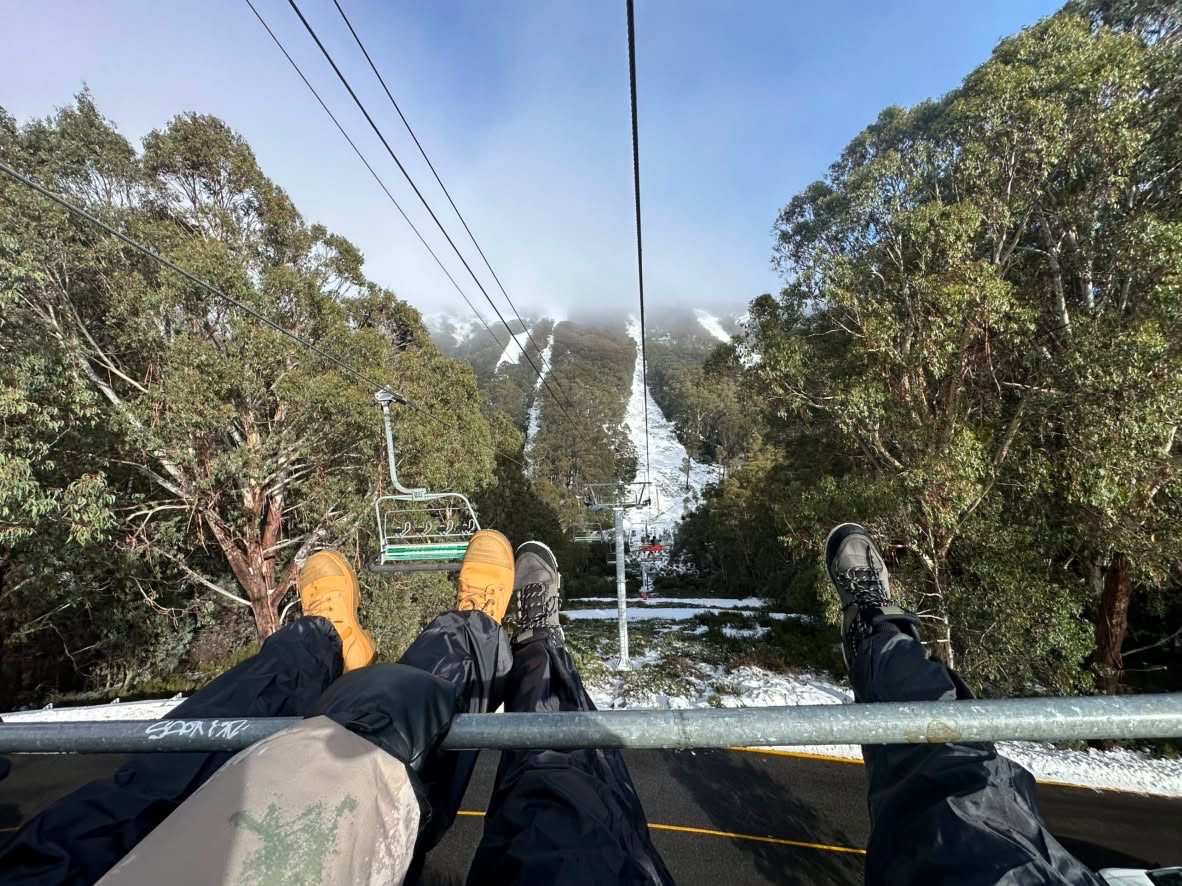Boots dangle from a chairlift above a snow-dusted mountain run, cables leading into the fog.