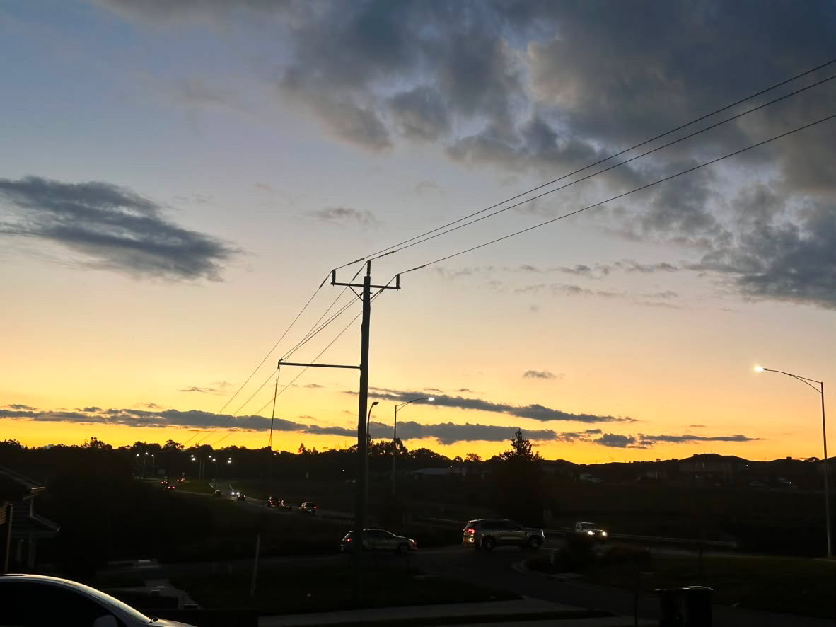 Car headlights trace a curve of road beneath power lines as the horizon glows orange at dusk.