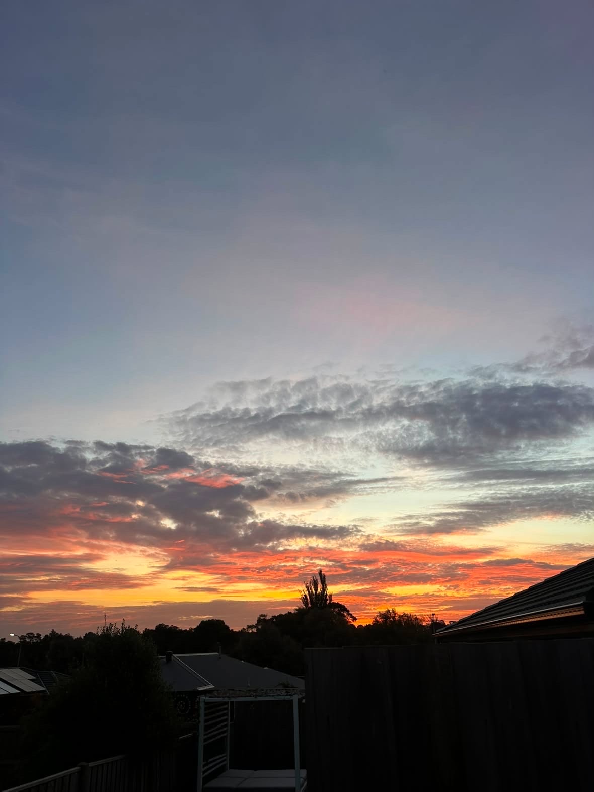 Soft pink and orange light drifts across a dusk sky above a quiet backyard pergola.