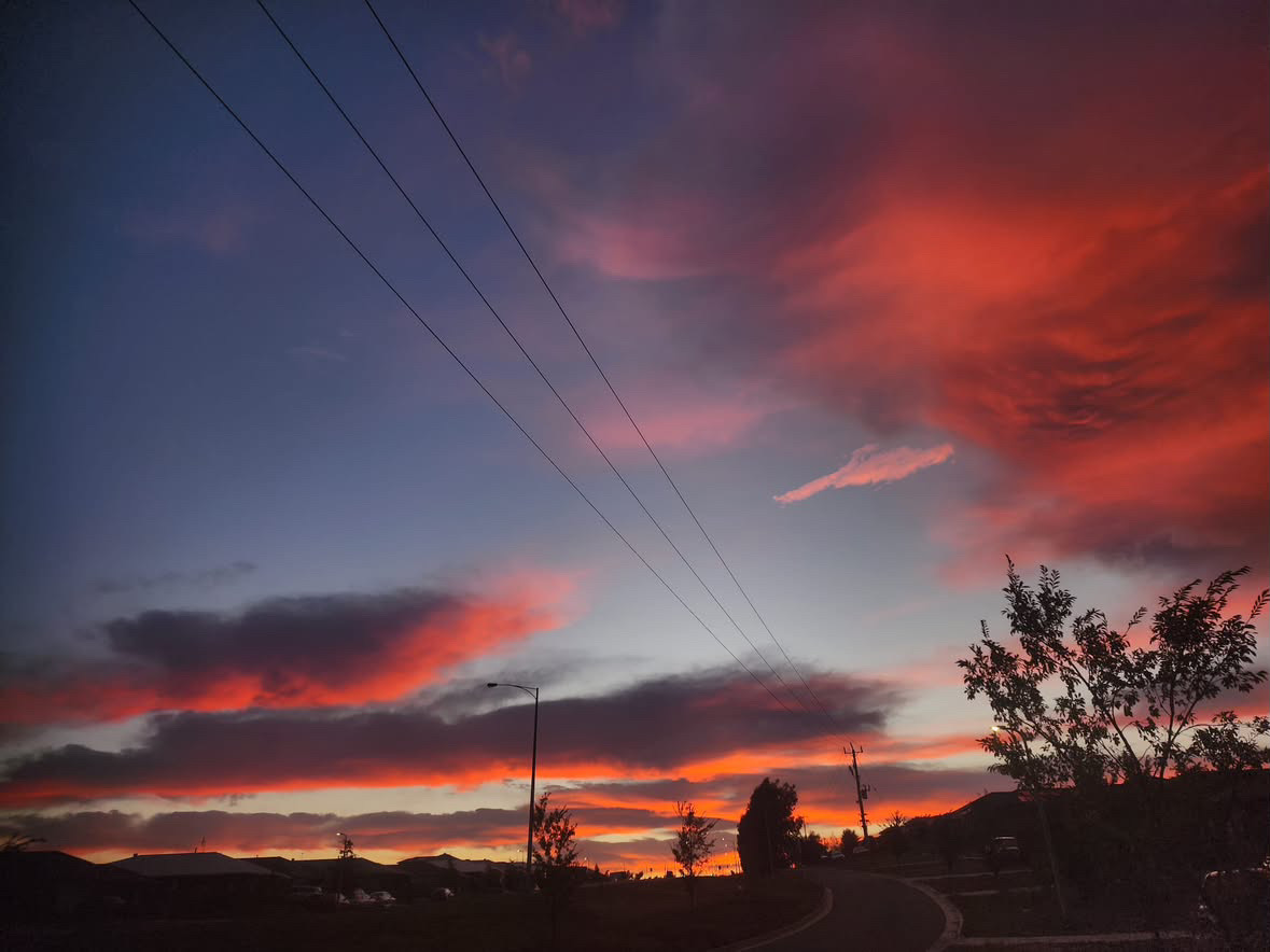 Streaked orange clouds fade into blue over a curving road and a lit streetlamp at dusk.