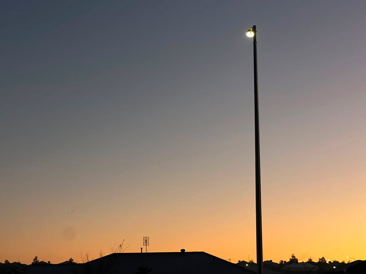 A single streetlamp glows against a gradient of dusk blue fading into amber at the horizon.